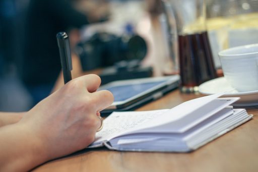 Persoon schrijft 's ochtends in een notitieboekje naast een kop koffie