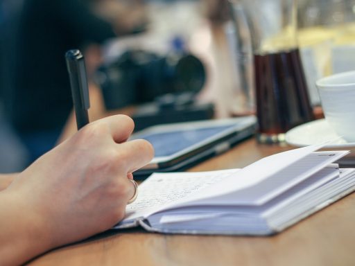 Persoon schrijft 's ochtends in een notitieboekje naast een kop koffie